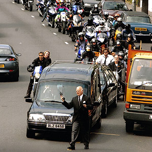 image of a large funeral cortege of motorcyclists behind a hearse